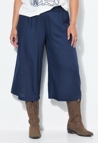 Marineblauwe wijde broek met een elastische tailleband en een gladde structuur, gecombineerd met bruine cowboylaarzen met decoratieve stiksels.