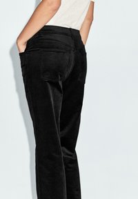 Pantaloni in corduroy neri con un design aderente, dotati di tasche posteriori, una texture liscia e vita alta, mostrati da una vista laterale.
