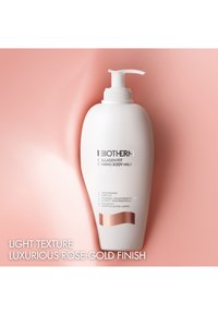 Vit plastflaska med pump och en roséguldfärgad accent, märkt "Collagen Fit Firming Body Milk," mot en mjuk rosa bakgrund.