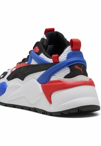Baskets Puma RS-X avec une tige en maille blanche, des superpositions noires, des accents bleus et rouges, et une semelle intermédiaire blanche épaisse avec des détails texturés.