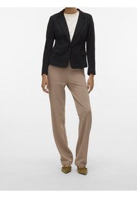 Zwarte blazer met een enkele knoop, twee voorzakken; beige, loszittende broek; olijfgroene platte schoenen met knoopdetail. Simpel, op maat gemaakt ontwerp.