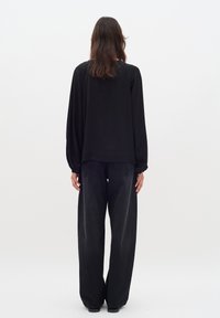 Blusa nera oversize con maniche lunghe, abbinata a jeans neri in denim a gamba larga. Tessuto morbido, design semplice, stile minimalista.