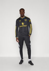 Black long-sleeve soccer kit with yellow accents, featuring a logo and "Snapdragon" text. Matching black pants with white side stripes.