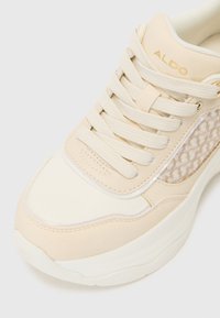 Sneaker beige in pelle liscia con dettagli in rete, punta rotonda, collo imbottito, lacci piatti e un sottile dettaglio del logo sulla linguetta.