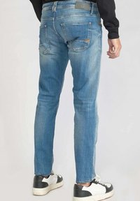 Jean slim bleu clair avec un délavage, cinq poches et de subtils détails de couture, associé à des baskets noire et blanche.