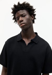 Polo shirt nero a maniche corte con colletto decorativo, realizzato in materiale di cotone, dotato di una vestibilità rilassata e dettagli superficiali testurizzati.
