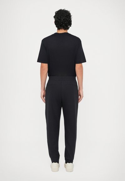 Czarny t-shirt z krótkim rękawem i ciemne spodnie o teksturowanym wykończeniu. Strój charakteryzuje się luźnym krojem, elastycznym paskiem w talii i tylnymi kieszeniami.
