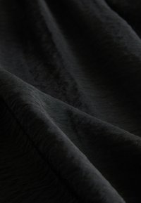 Mjuk, svart tyg med en texturerad yta, med lätt glans och mjuka vågor. Materialet verkar vara lätt och faller lätt.