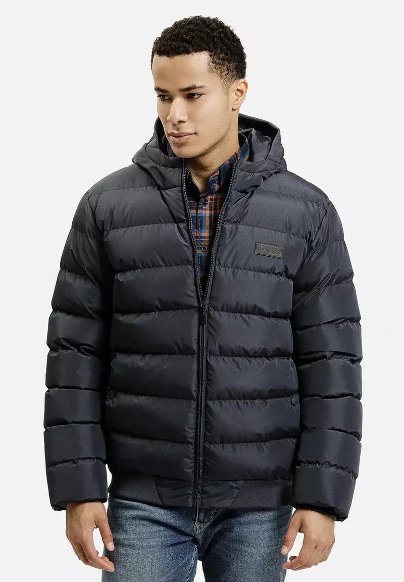 Kurtka puchowa w ciemnym granacie, z kapturem, pikowanym wzorem, zamkiem błyskawicznym z przodu i elastycznymi mankietami. Noszona na koszuli w kratę na guziki.