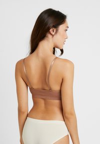 Brun ribbet bh med tynne stropper, justerbar baklukking, paret med lyse kremfargede truser. Glatt tekstur og tettsittende design.