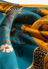 Écharpe en soie avec un tissu bleu et jaune doré, ornée de motifs floraux et léopard. Texture douce avec des détails complexes.