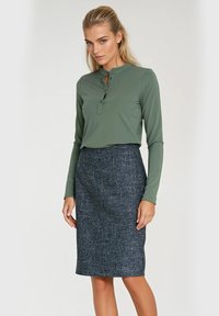 Zielona koszula z długim rękawem i dekoltem henley z trzema guzikami, zestawiona z fakturowaną ciemnoniebieską spódnicą ołówkową.