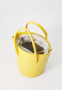 Sac seau en cuir jaune avec deux poignées, un extérieur texturé et une doublure en tissu gris. Fermeture à cordon avec un intérieur doux.