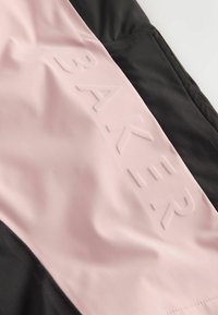 Juodos ir rožinės sportinės aprangos medžiaga su tekstūruotu, iškilios "BAKER" logotipu rožiniame panele ir lygiomis juodomis detalėmis.