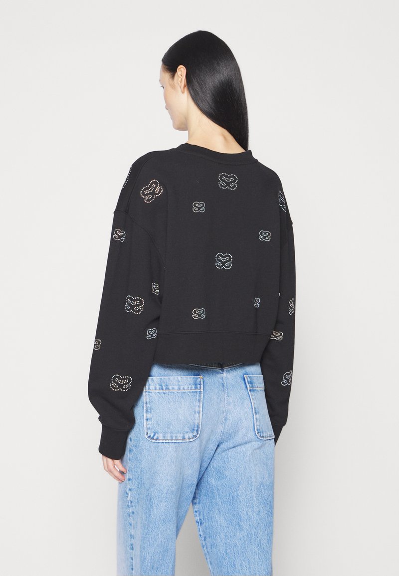 Schwarzer, taillierter Sweatshirt mit langen Ärmeln, verziert mit mehrfarbigen Strasssteinen in verschiedenen Formen, kombiniert mit hellblauen Jeans.