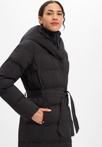 Zwarte donzen jas met een brede capuchon, een getailleerde taille en lange mouwen. Heeft diagonale doorgestikte patronen en zijzakken. Licht glanzende stof.