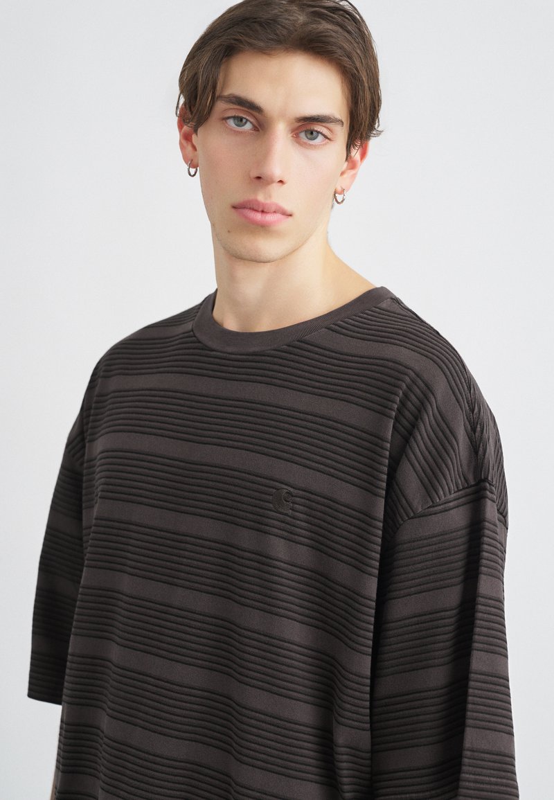 Camiseta de manga corta de color marrón oscuro con rayas, que presenta una textura acanalada, un cuello redondo y un pequeño detalle de logo en el pecho.