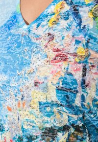 Bluzka z dekoltem w serek, w niebieskim i wielokolorowym wzorze abstrakcyjnym, ozdobiona małymi cyrkoniami dla tekstury i detalu. Miły w dotyku materiał.