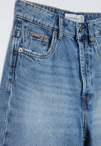 Lyseblå, højtaljede denimjeans med en tekstureret overflade, der har kobberhardware og en lille frontlomme. Størrelsesmærket er synligt.