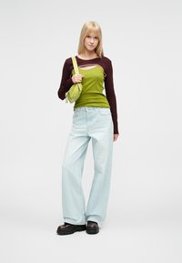 Top de manga comprida verde e bordô, jeans de perna larga azul claro, botas pretas com plataforma e uma pequena bolsa verde a tiracolo. Fundo simples.