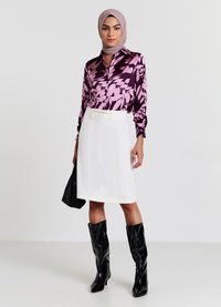 Seidenbluse mit einem lila und rosa Blattdesign, kombiniert mit einem weißen Bleistiftrock mit Gürtel und vertikalen Nähten, schwarzen kniehohen Stiefeln.