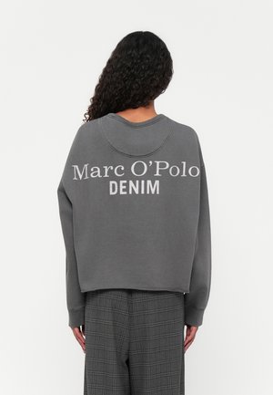 Grijze sweatshirt met ronde hals, drop shoulders, en witte "Marc O'Polo DENIM" op de achterkant gedrukt. Draagt een grijze geblokte broek.