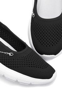 Schwarze Netzschlupfschuhe verfügen über ein strukturiertes Obermaterial, eine weiße Gummisohle und eine kleine Kettenakzentuierung an der Seite, die einen engen Sitz bieten.