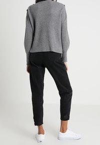 Grijze geribbelde trui met een losse pasvorm, gecombineerd met zwart taps toelopende jeans met versleten zoom, en witte sneakers.