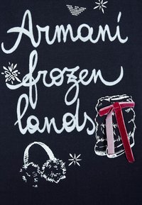 Černá tkanina s bílým vyšitým textem „Armani frozen lands“, s kožešinovými prvky a sametovými stužkami na válcovém tvaru.