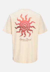 Loose-fitting cream t-shirt featuring a pink sun graphic with spirals and text "Byron Beach JACK&JONES" at the bottom. Cotton material.