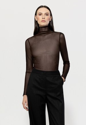 Brown sheer long-sleeve top with a high neck, featuring embellishments. Paired with tailored black pinstripe trousers.