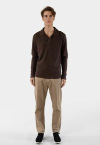 Brun ribbad långärmad polo med krage, tillsammans med beige byxor och svarta sneakers. Enkel, avslappnad design med texturerad tyg.