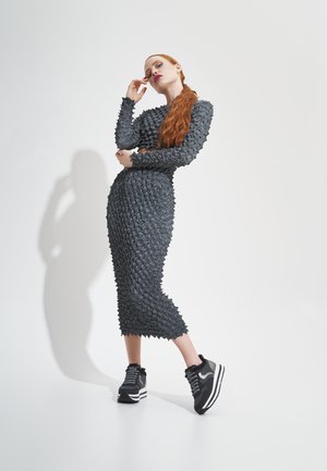 Black textured dress with a fitted silhouette and protruding details, paired with black and gray sneakers featuring white stripes.