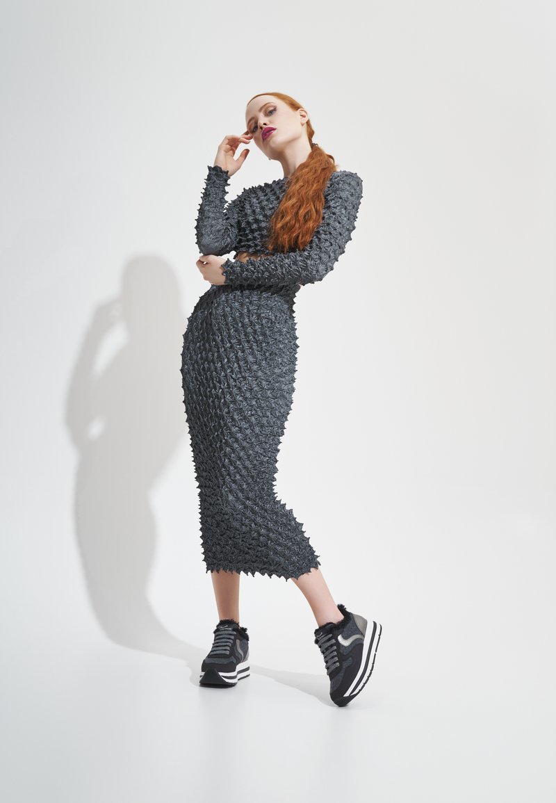 Robe noire texturée avec une silhouette ajustée et des détails saillants, associée à des baskets noires et grises avec des rayures blanches.