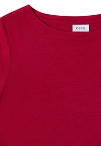 Czerwona koszulka z krótkim rękawem, wykonana z miękkiego, teksturowanego materiału. Posiada okrągły dekolt oraz małą metkę z napisem "CECIL" blisko kołnierza.
