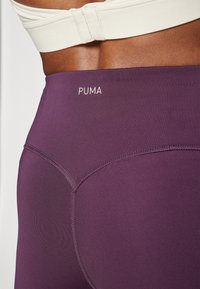 Lila sport leggings sima textúrával és varrott díszítésekkel, fehér "PUMA" logóval a derékpánton.