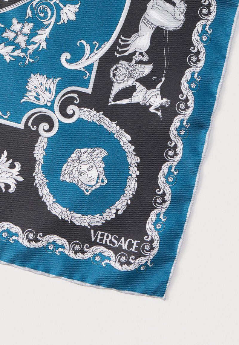Silk scarf corner with black and teal background, white floral patterns, Medusa head emblem, chariot illustration, and "Versace" logo.
