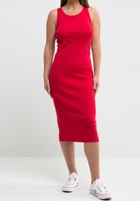 Robe midi rouge à rayures avec un col rond et sans manches, associée à des baskets blanches basses. Texture lisse et silhouette ajustée.