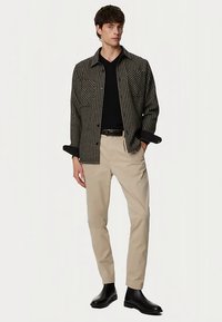 Koszula na guziki w czarno-białym wzorze jodełki, w połączeniu z beżowymi spodniami i czarnymi botkami. Widoczne dwie kieszenie na piersi.