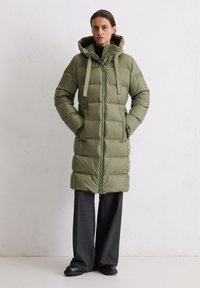 Gevoerde olijfgroene jas met een capuchon, ritssluiting en twee zijzakken; beschikt over brede horizontale stiksels en een strik bij de nek.