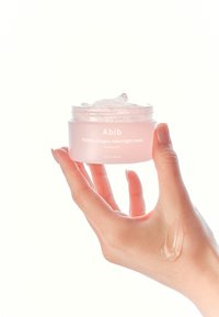 Maschera notturna al collagene PDRN in un barattolo trasparente e rotondo con una sfumatura rosa. Si vede la consistenza gelatinosa, tenuta in una mano con una piccola quantità sulla pelle.