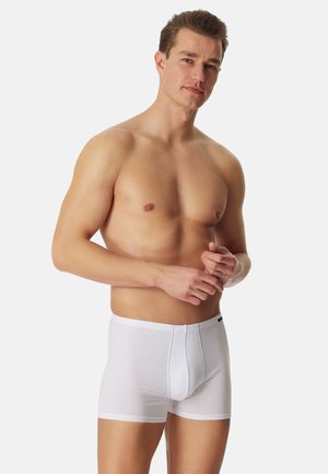 White cotton boxer shorts with a fitted design, elastic waistband, and contrasting stitching, displayed on a model with a neutral background.