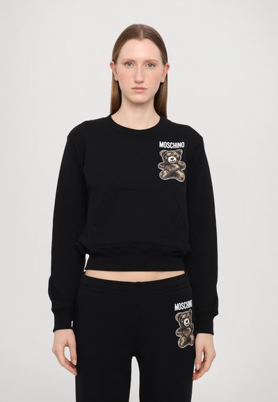 Černá mikina se zlatním motivem medvídka a textem "MOSCHINO" na hrudi. Má kulatý výstřih a přední kapsu. Materiál je směsí bavlny.
