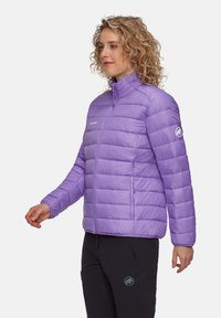 Lila puffjacka med hög krage, zigzag-söm och frontdragkedja. Har en logotyp patch på ärmen och är tillverkad av lätt material.