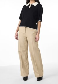 Czarna bluzka z krótkim rękawem z białym kołnierzykiem i zapięciem na guziki. Beżowe spodnie o wysokim stanie i szerokich nogawkach. Czarne buty z noskiem w szpic.