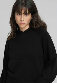 Sweat à capuche noir en tissu doux avec une poche kangourou à l'avant et une coupe décontractée. Comprend des poignets et un ourlet côtelés.