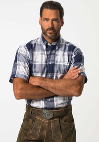 Košile s krátkým rukávem v kostičkovaném vzoru v námořnické modré a bílé barvě, v kombinaci s tmavě hnědými lederhosen s dekoračními švy a kovovou přezkou.