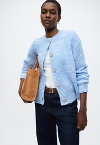 Ανοιχτό μπλε πλεκτή ζακέτα με ριμπ λεπτομέρειες, στρογγυλή λαιμόκοψη και κλείσιμο με κουμπιά; συνδυασμένη με σκούρα τζιν και τσάντα από καφέ σουέντ.