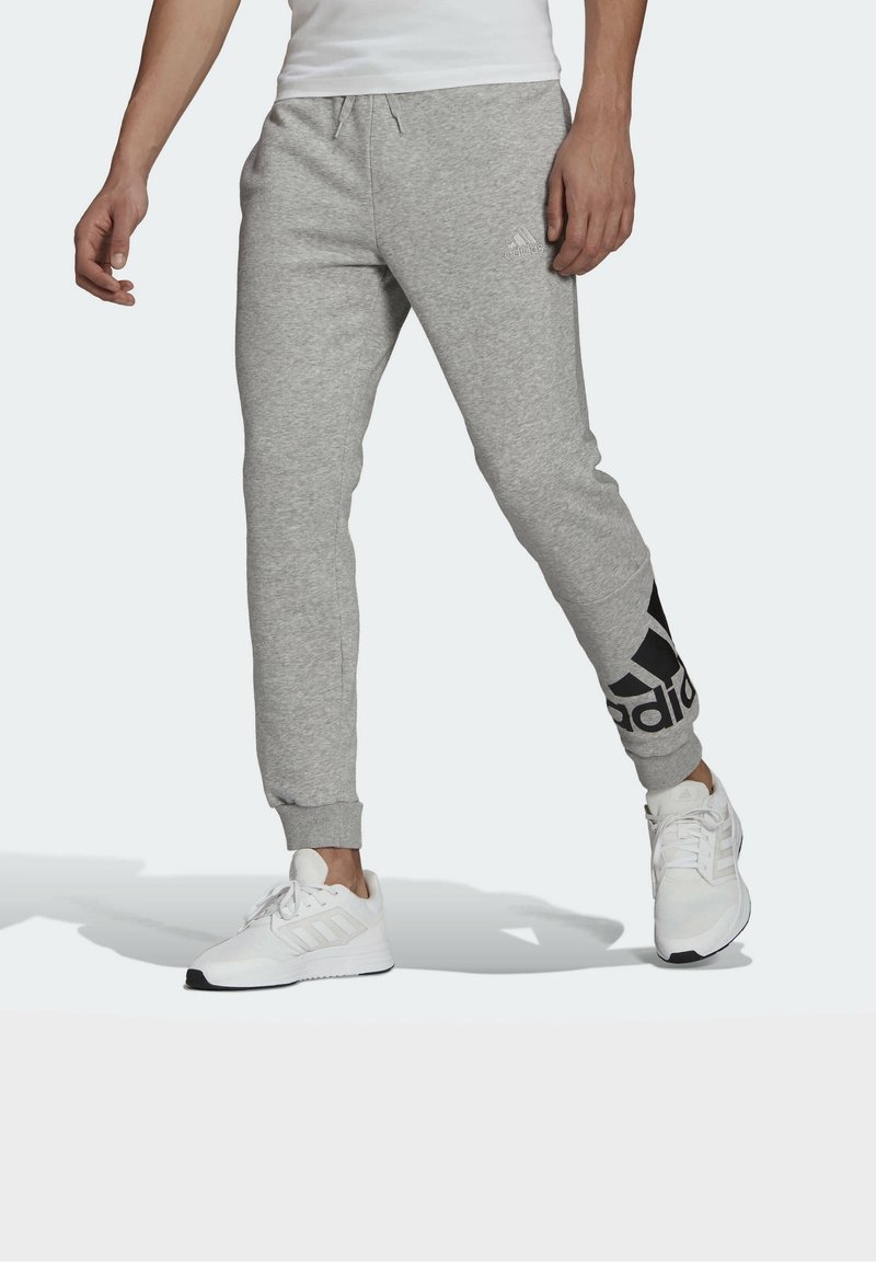 Szare dresy o zwężanym kroju, z elastycznym paskiem w talii i czarnym logo Adidas na lewym nogawce. Noszone z białymi butami sportowymi.