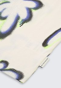 Tissu multicolore avec des motifs abstraits bleus, verts et noirs sur une base blanche ; présente une étiquette Tom Tailor dans le coin inférieur.
